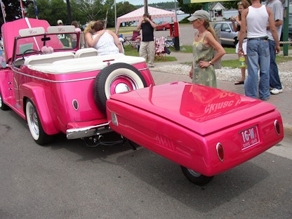 A pink collector vehicle and trailer parked on the side of the road, with passerby taking photos.
