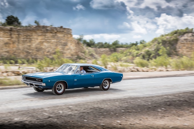 Blue classic Charger speeding down desert highway with trees in background