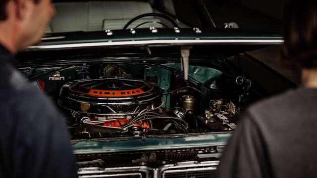 two men looking into the engine of a classic car