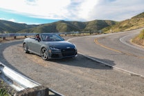 A grey Audi TT convertible is parked on the side of the road overlooking the mountains.