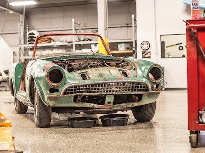 A green collector car without headlights, doors, or hood, being restored in a garage