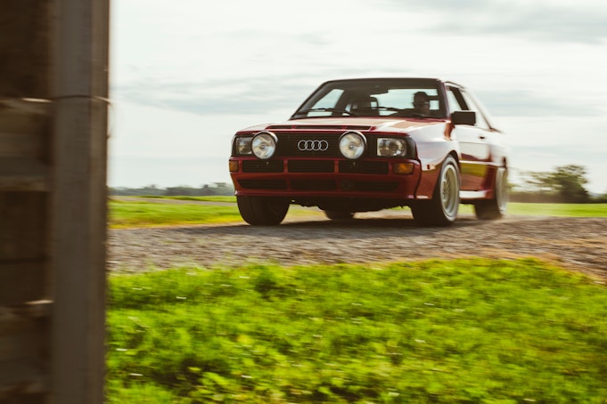 A red classic Audi sedan drives on a gravel country road.