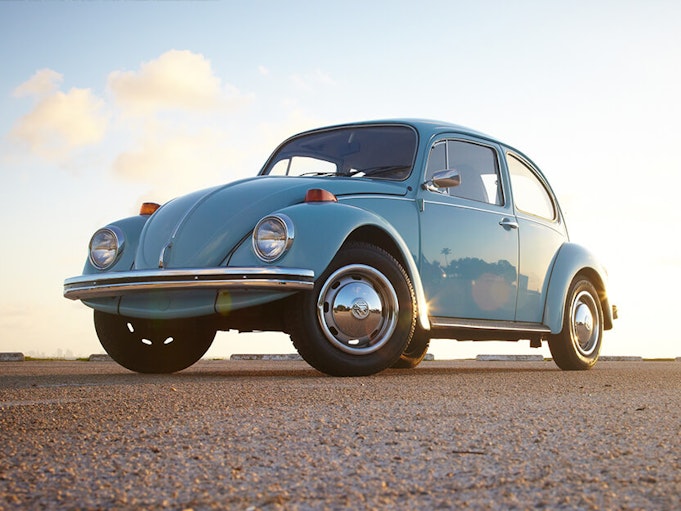 A sky blue collector Volkswagen Beetle parked on concrete, with blue sky in the background.