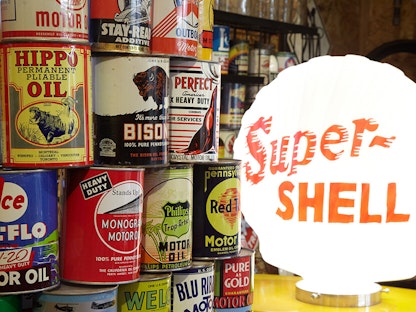 A stack of vintage oil cans by a lamp, with shelves of oil cans in the background.