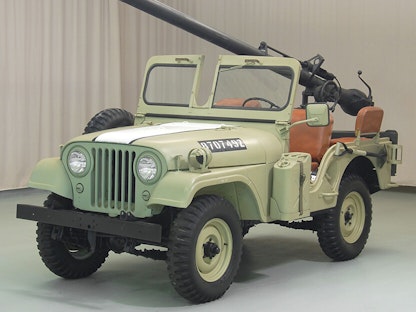 A green collector military jeep with a mounted gun, parked indoors.