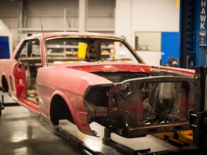 A red collector car with just a frame and fender, being restored in a garage