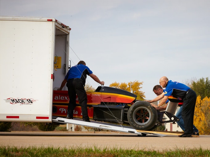Three men pushing a collector race car into a trailer.