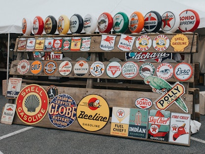 Vintage signs for beverages and car parts behind an array of antique collectibles like cans of axle grease and figurines.