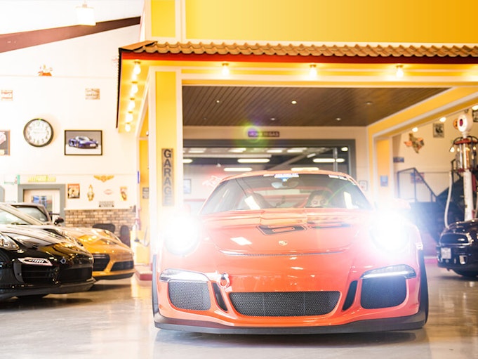 An orange car with lights turned on sits inside a large garage.