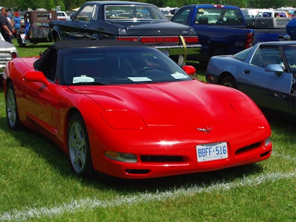 Red collector convertible parked on a grassy lot by other classics.