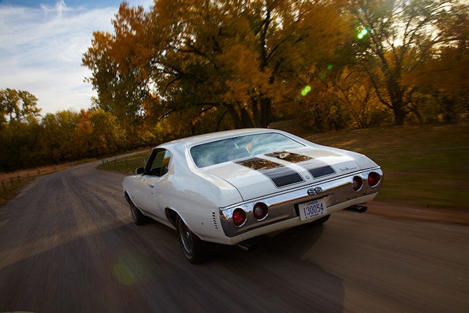 Back view of classic white Chevelle driving in to sunset